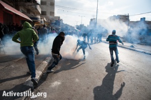 A Palestinian youth with a gas mask grabs a tear gas grenade fired by Israeli forces during clashes in the West Bank town of Bethlehem protesting Israeli attacks on Gaza, November 20, 2012. (photo: Ryan Rodrick Beiler/Activestills.org)
